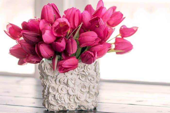 Here is a vase made of cement but has a design in it to look like roses and there are dark pink tulips in it.