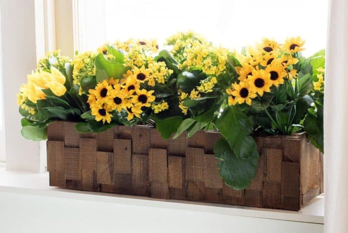 A rectangular box made of wood with pretty yellow plants in it.