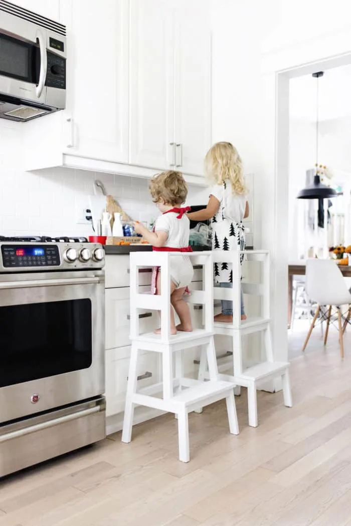 IKEA Hacks, two little girls standing on stools modified so they are safe working at the kitchen counter.