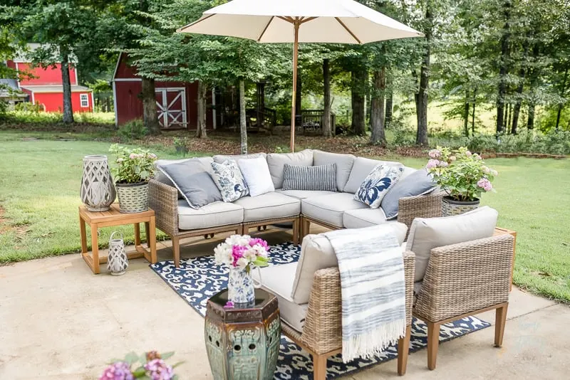 A sectional sofa and chairs on a relaxing patio with an umbrella and blue and white rug.