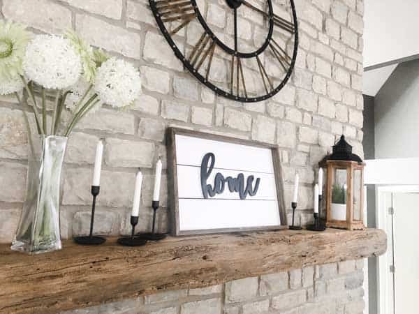 A shiplap sign on the mantel with shiplap and the word home on it.