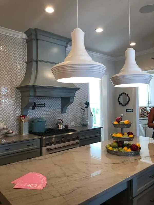 A kitchen with two white pendant lights over the island and a gorgeous french blue oven hood.