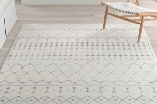 A white rug with gray geometric shapes on a light wood floor.