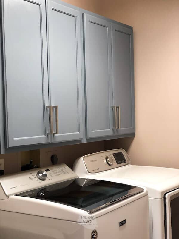 A laundry room with cabinets above the washer and dryer with silver cabinet pulls.