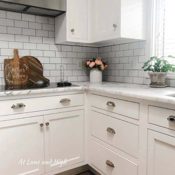 A white kitchen with silver knobs and pulls, white carrera countertops and white subway tile backsplash.