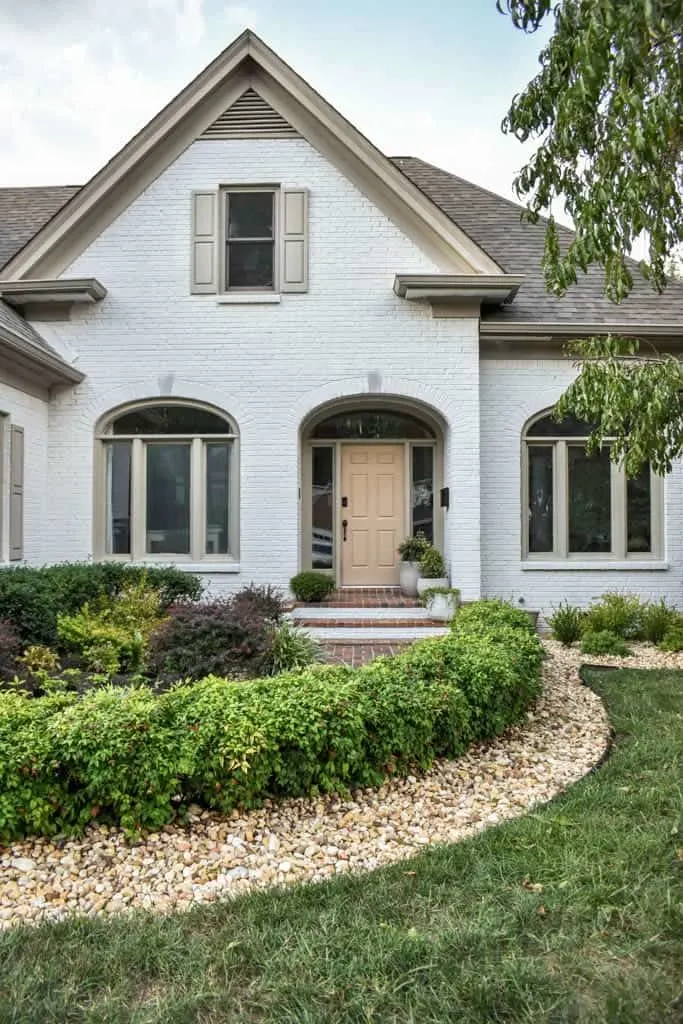 The front of a brick house that is painted white and has a light peach colored door.