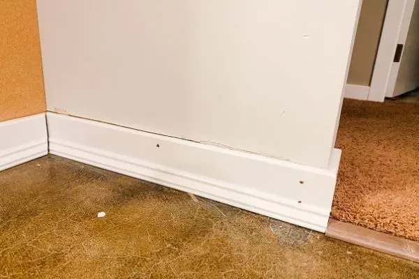 This shows re-installing the baseboards on the wall on the ends of the cabinets.