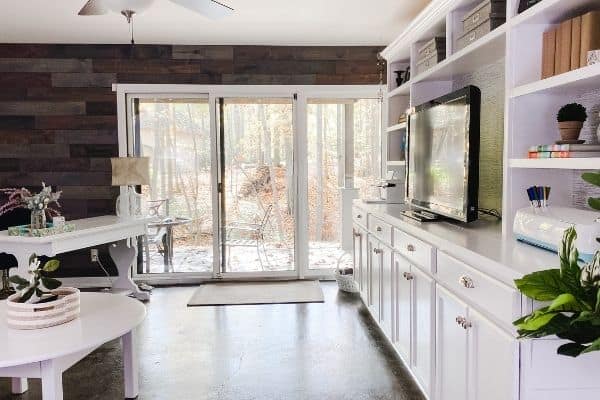 The reclaimed wood wall surrounding a sliding glass door and a white desk next to it, with built-ins on the wall perpendicular the wood accent wall.