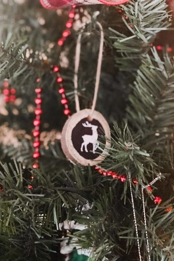 Tree slice ornament with a silhouette of a reindeer on it hanging on a Christmas tree.