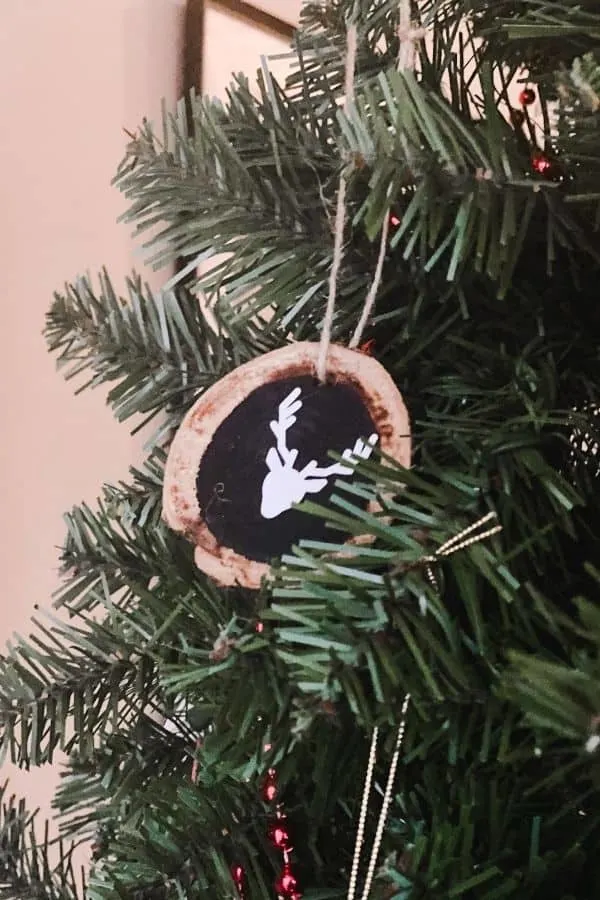 Tree slice ornament with a reindeer on it hanging on a Christmas tree.