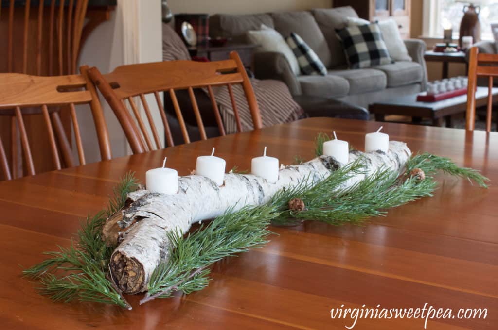 A birch log with holes drilled in for candles and pine sprigs on a dining table.
