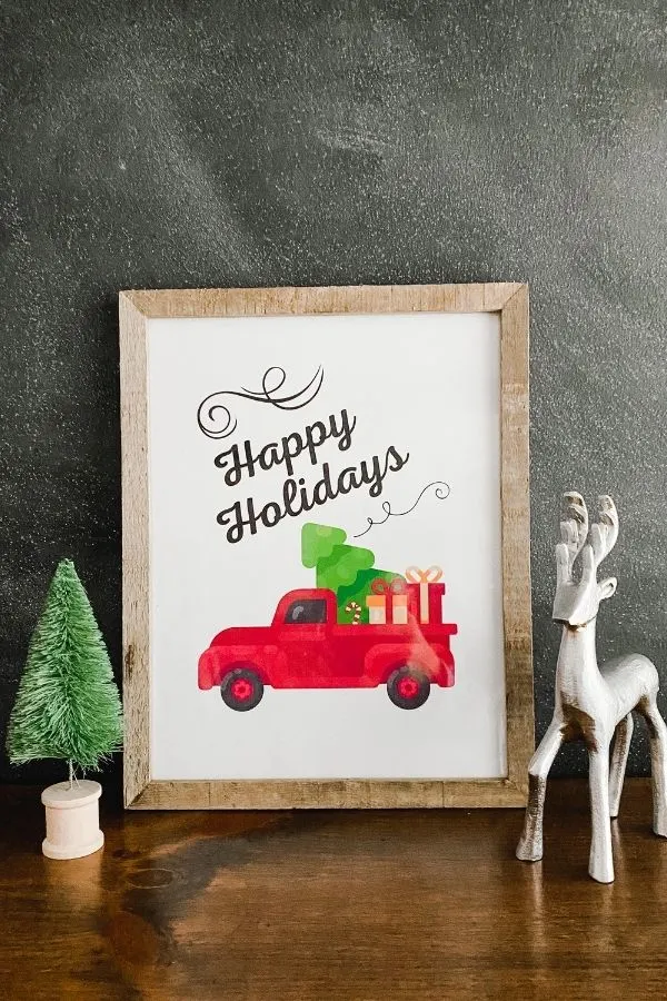 A farmhouse Christmas printable that says Happy Holidays with a red old truck and a christmas tree and packages in the bed of the truck.
