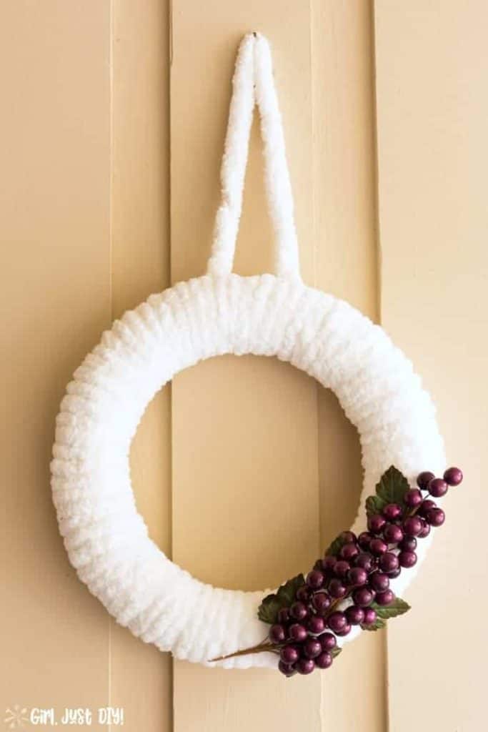 A wreath made with fuzzy white yarn and grapes on it.