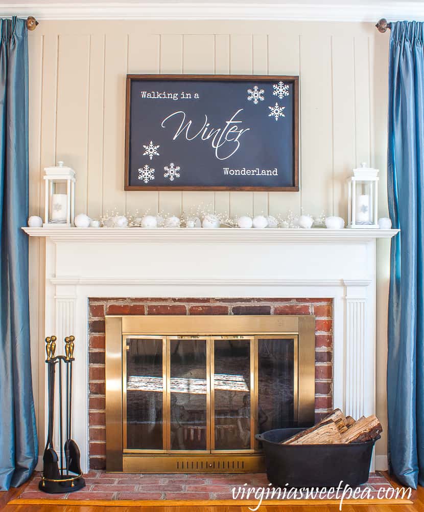 A mantel with all white decor and a sign on the wall that says walking in a winter wonderland.