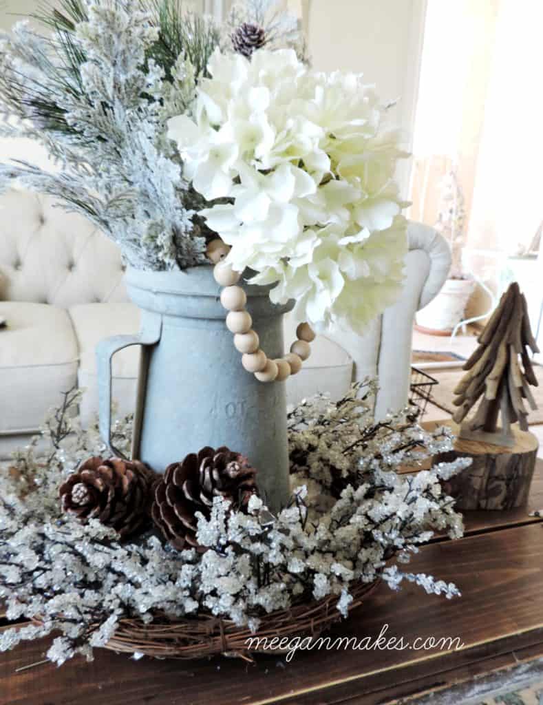 A vignette on a coffee table of a blue vintage pitcher and faux flowers and pinecones on a basket.