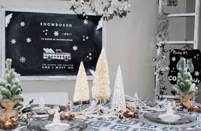 A winter table setting with pine trees and a snowboard chalk board on the wall.