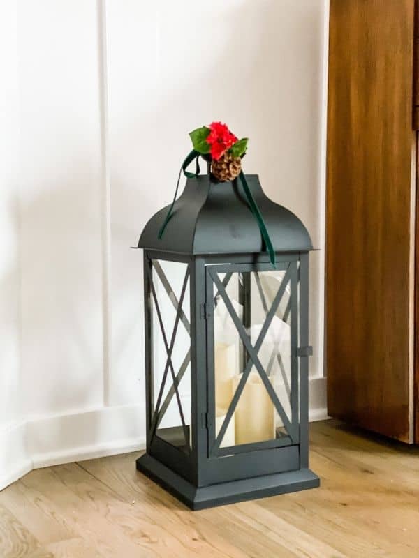 A lantern with a sprig of greenery on top with a green velvet ribbon.