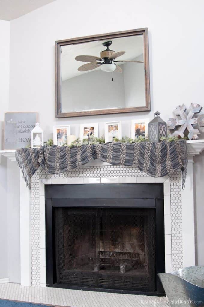 A mantel with family photos, a snowflake made of wood and fabric draped across it.