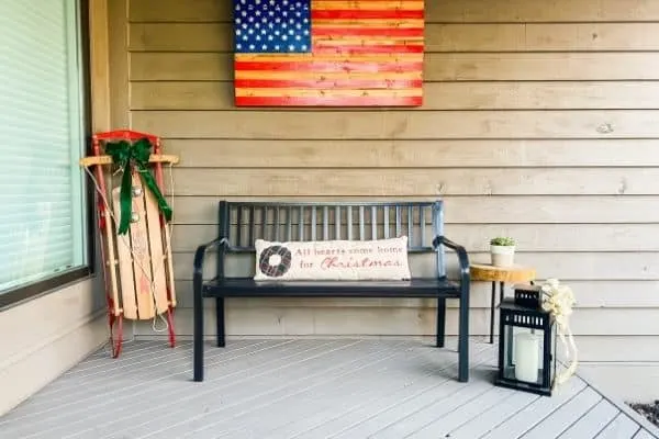 The front porch bench with a long lumbar pillow and a sled with a bow.