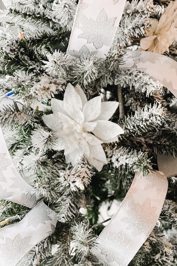 A closup of the flocked Christmas tree with white poinsettias and white ribbon with silver poinsettias on it.