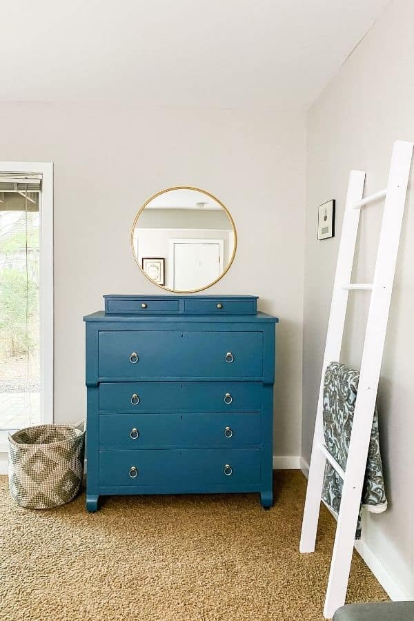 Guest bedroom dresser with the round mirror and woven basket next to it.