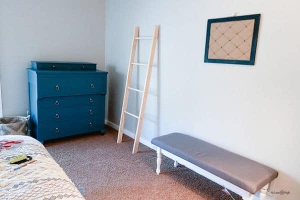 Agreeable Gray on the walls and a bright blue dresser, a blanket ladder and a bench on brown carpet.