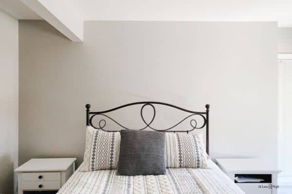 The headboard wall before the herringbone wall stencil with a black iron bed and boho style bedding with white nightstands.