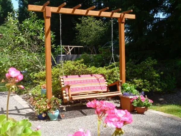 A bench swing hung from a pergola with flower pots all around.