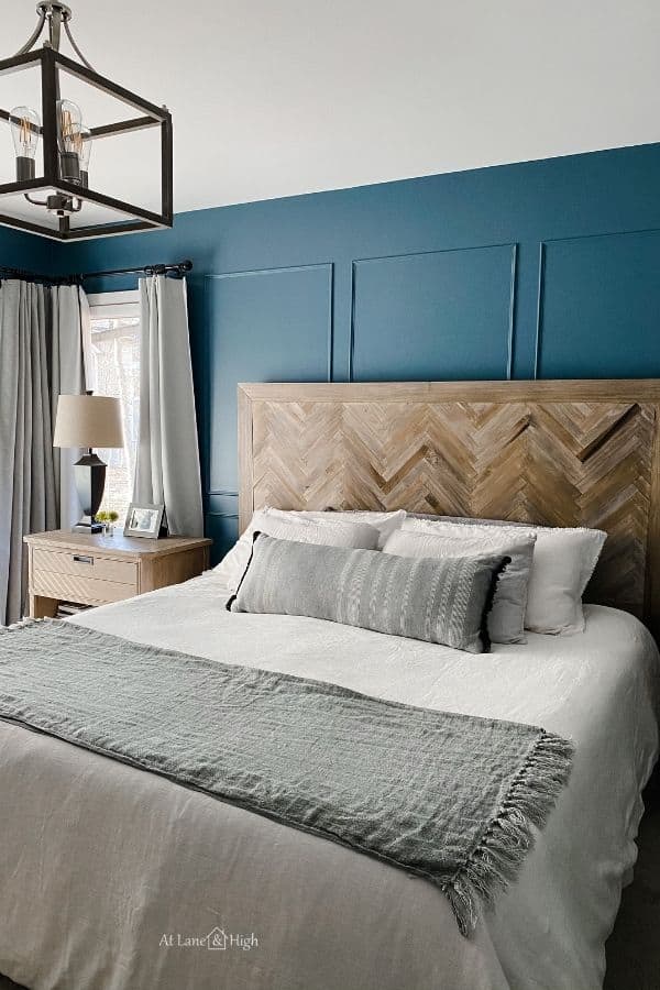 A bed with a herringbone headboard, blue walls and white bedding with a throw blanket at the foot of the bed.