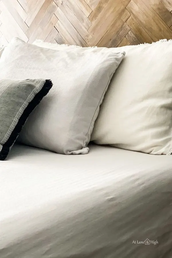 The new bedding with white shams, gray sheets and a dark gray lumbar pillow in front all agains the herringbone headboard.