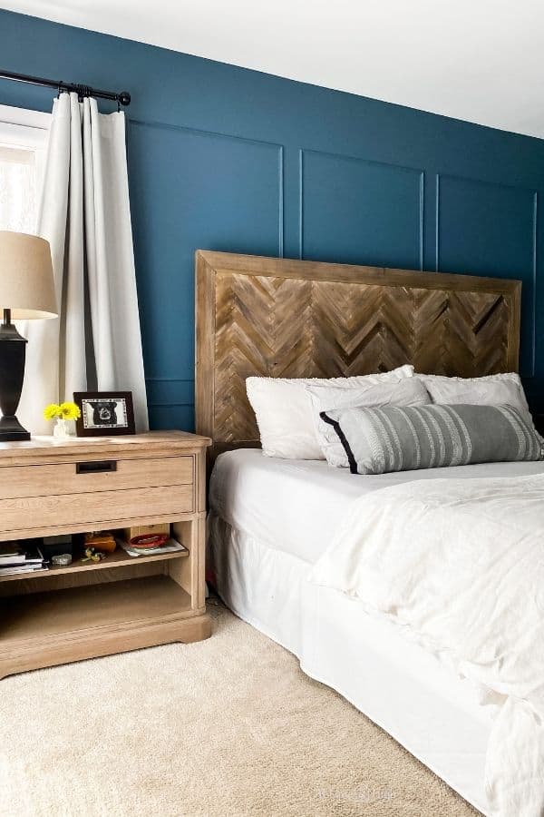 A bedroom with a herringbone headboard, whtie bedding, and. medium blue walls.