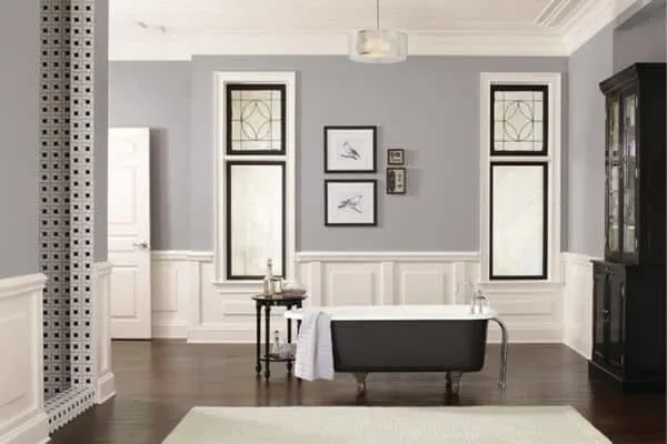 Passive used on the wall sin a bathroom with dark wood floors, white wainscoting and black trimmed windows.