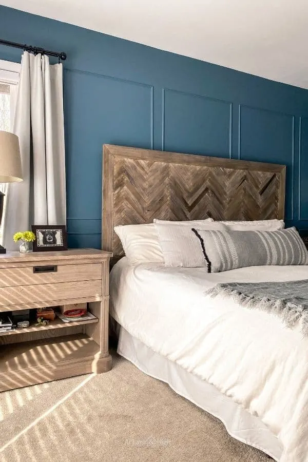 A bed with a herringbone headboard, white bedding, picutre molding on the walls that are painted smokey blue.