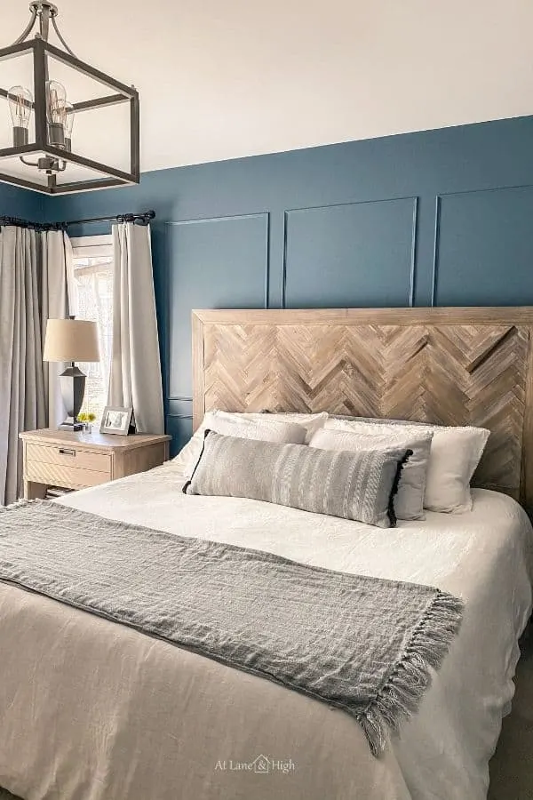 A bedroom with dark blue walls and a herringbone headboard with white bedding.