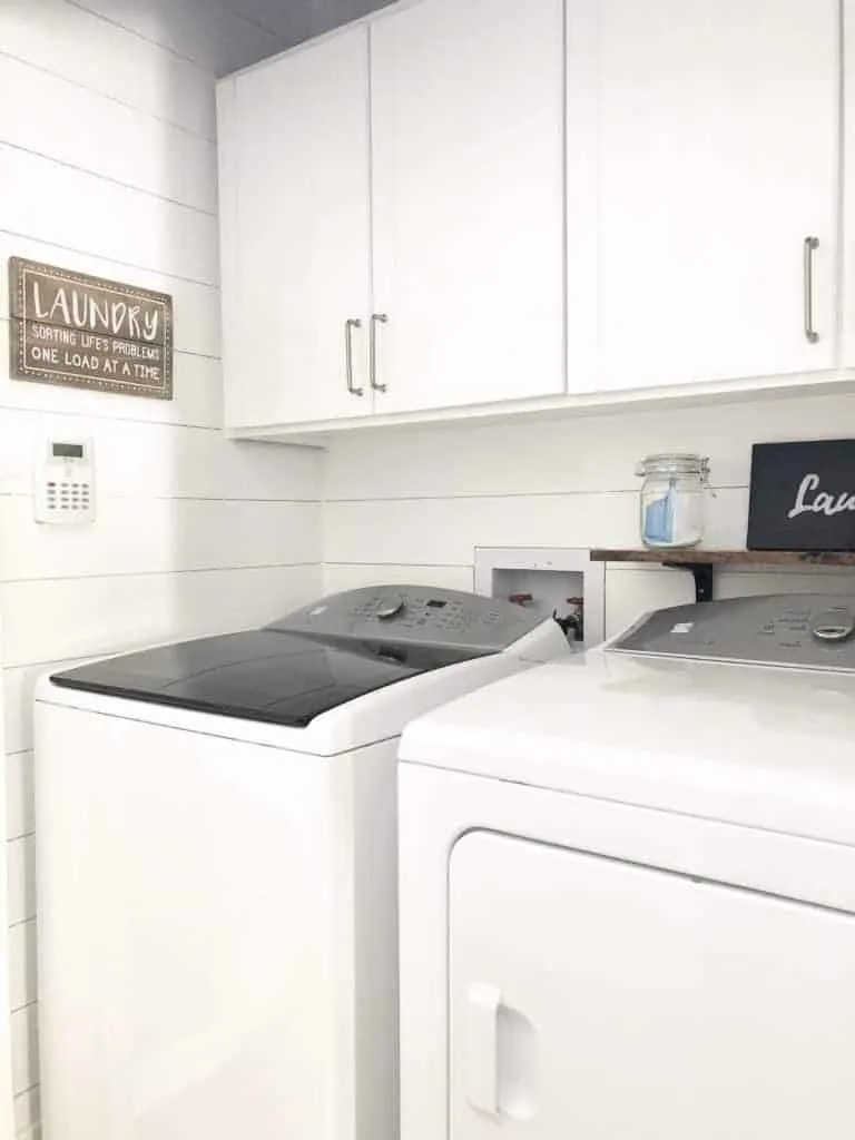 A laundry room with white painted shiplap walls and white cabinets.