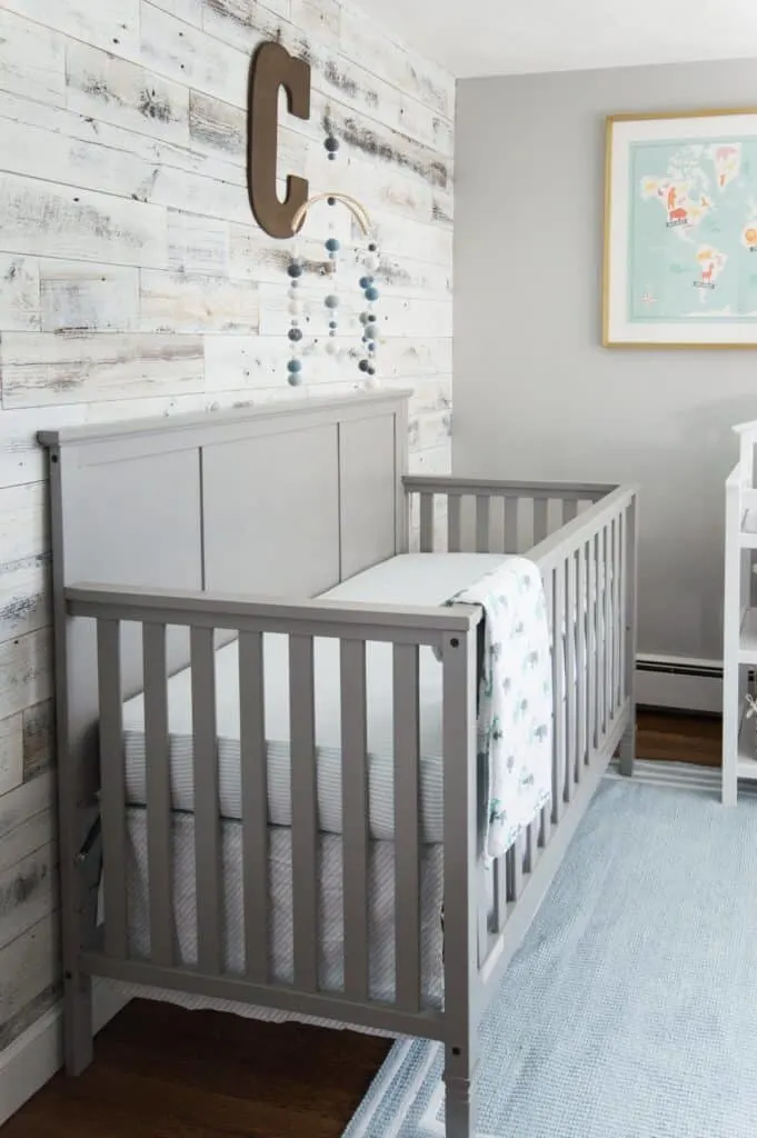 A nursery with a gray crib that matches the Stonington Gray walls and a white washed reclaimed wood wall.