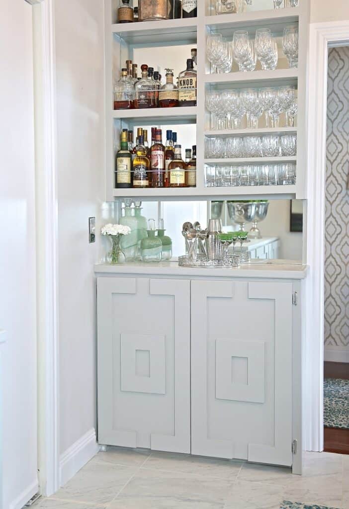 A bar with medium gray paint and mirror on the wall behind the glasware.