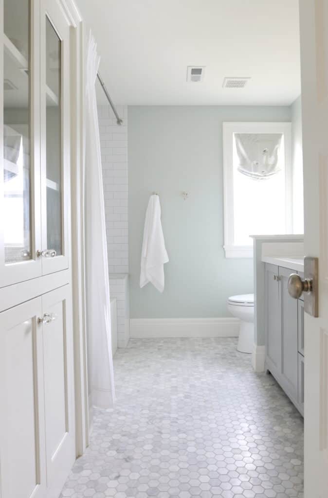 A pretty bathroom with Sherwin Williams Sea Salt on the walls, white cabinetry, marble mosaic floor and white subway tile in the shower.