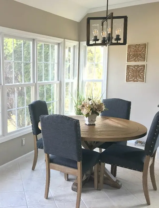 A dining table with navy blue upholstered chairs, tons of windows and a flower arrangement on the table.