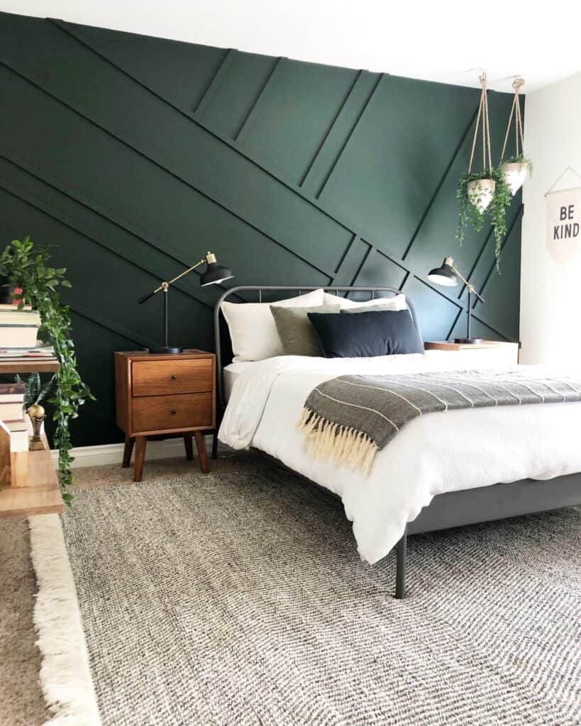 An accent wall of Essex Green behind a metal bed and wood night stand with lots of hanging plants.