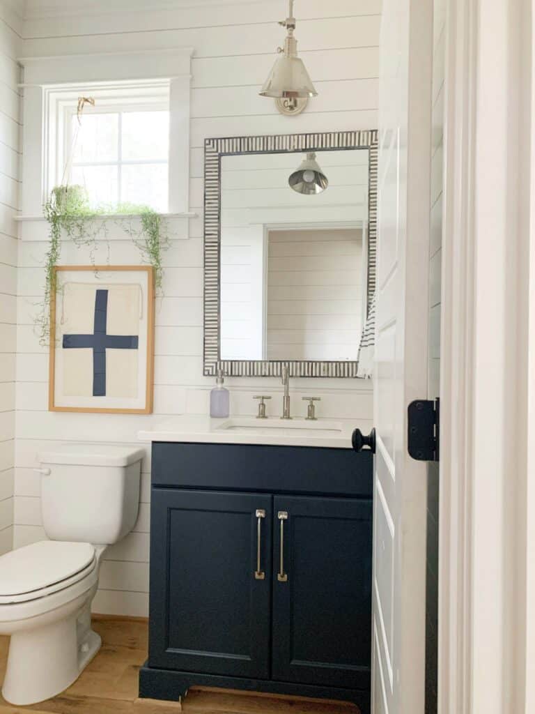 This powder room has white shiplap walls with a vanity painted in dark blue.