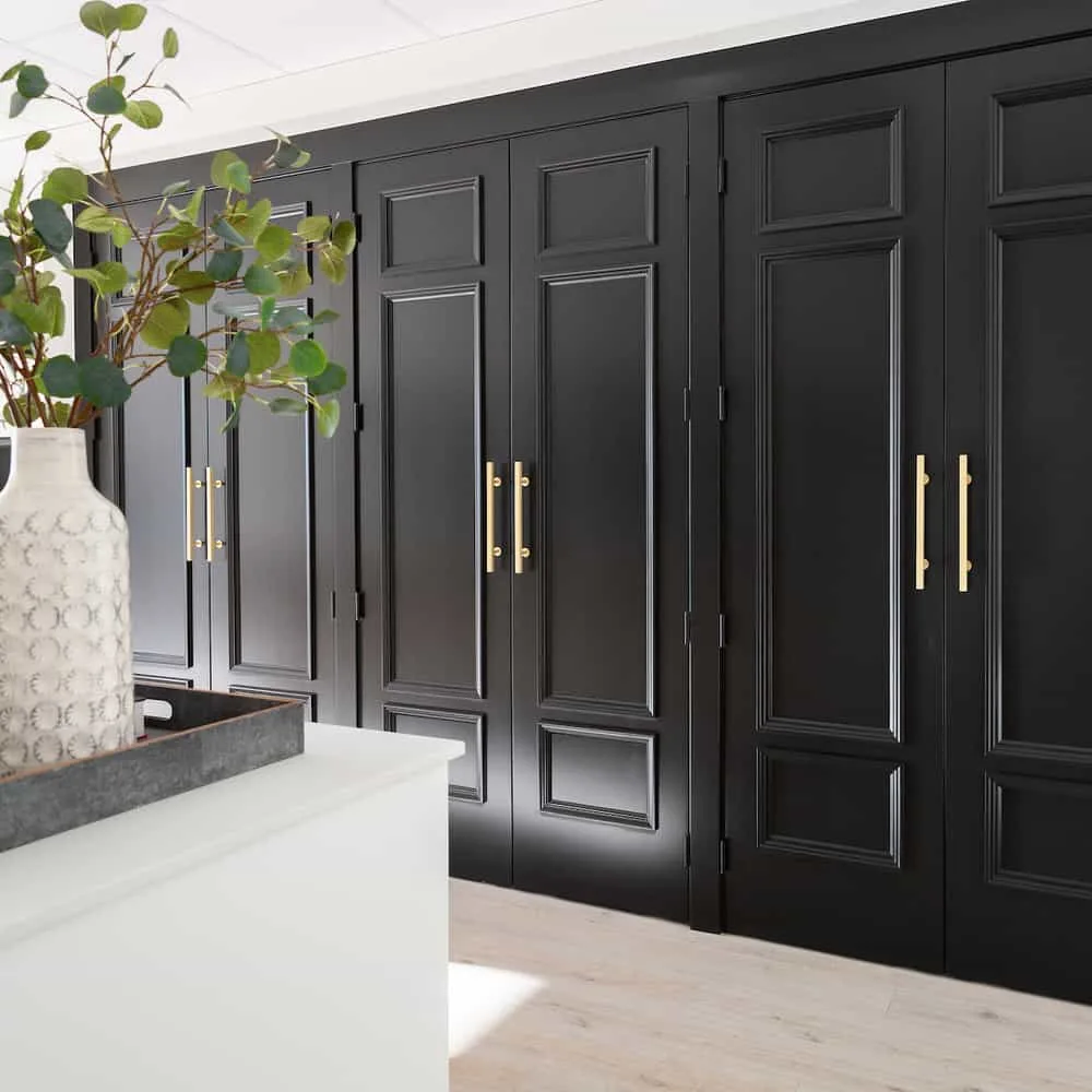 A wall of cabinetry with doors that are painted jet black and have gold oversized door handles.
