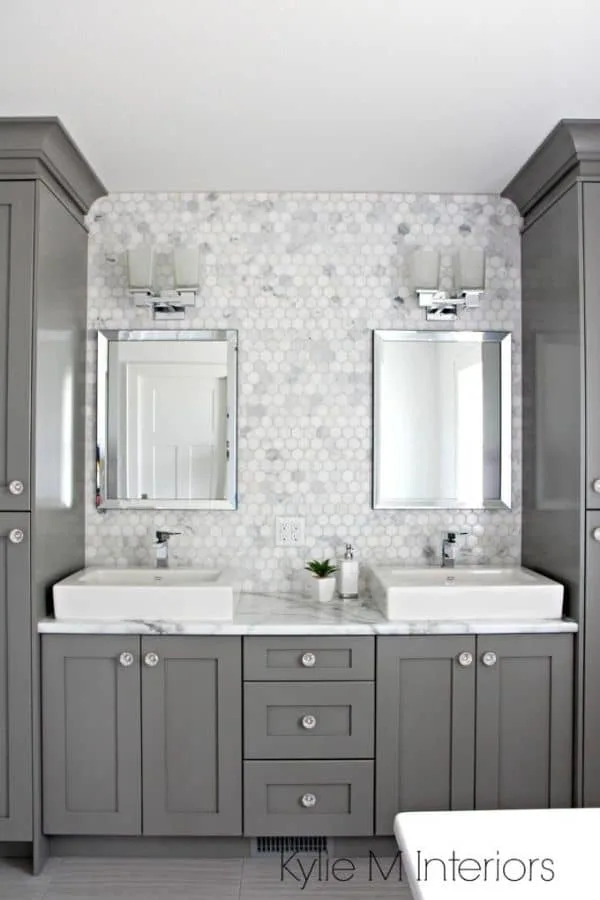 Benjamin Moore Chelsea Gray paint on bathroom cabinets with crystal knobs and carrera marble mosaic tile on the wall behind the white sinks.