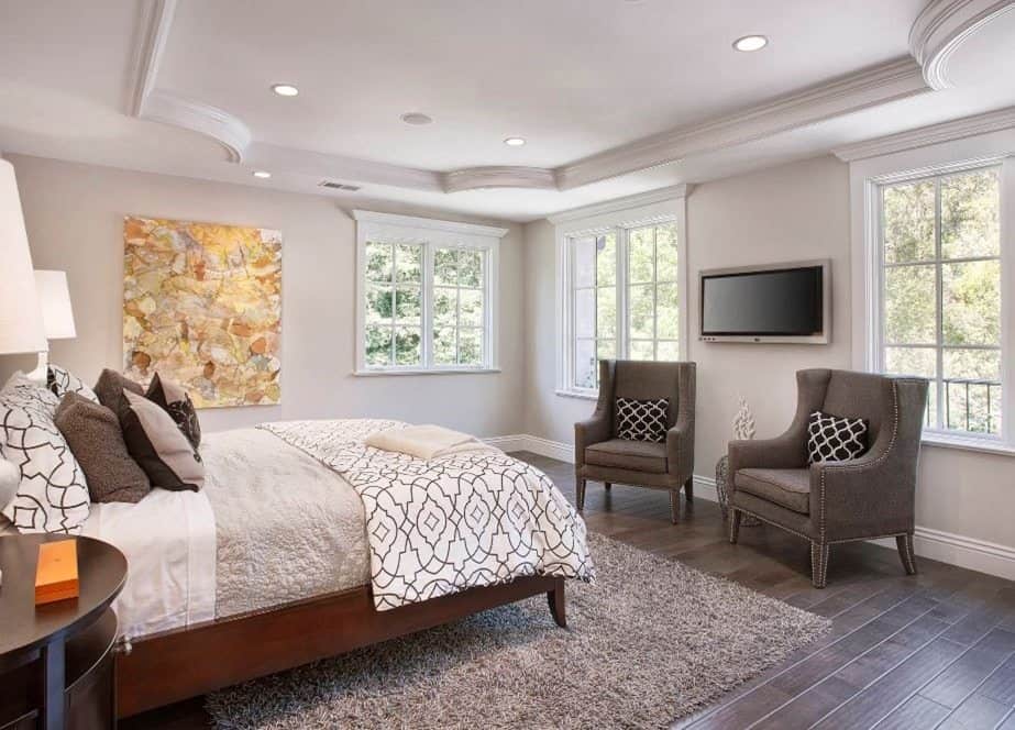 This is a bedroom with wood floors, gray sitting chairs and a wood framed bed.