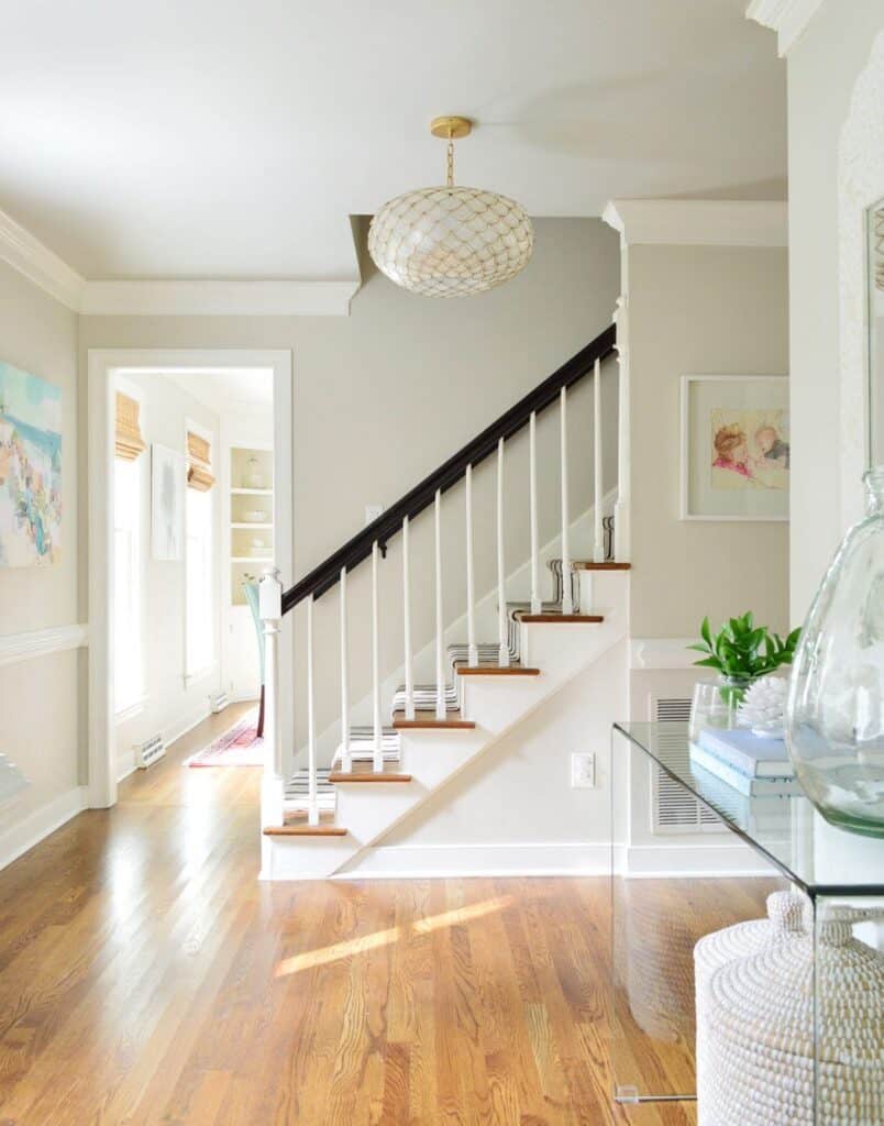 An entryway with medium toned wood floors, Edgecomb Gray on the walls and a staircase in white and dark stain.