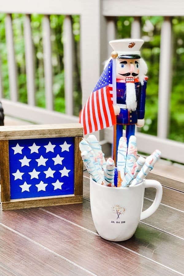 A farmhouse sign with with stars on it next to a Marine nutcracker and chocolate covered pretzel rods.