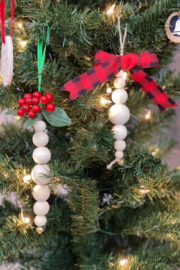 Two wood bead ornaments, one with green ribbon and berries at the top and the other made with twine and a red and black bow.