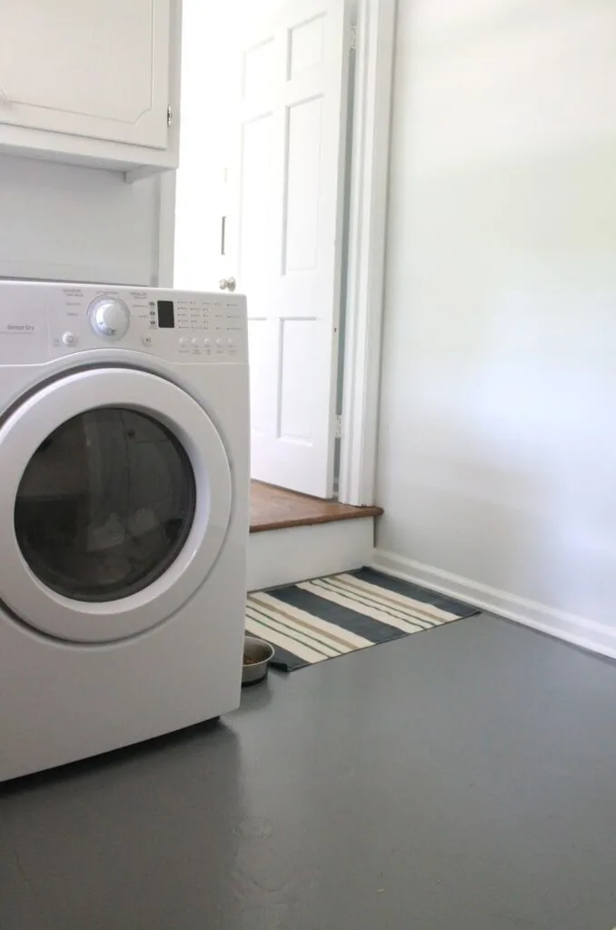 A laundry room with gray painted concrete and a blue and white striped rug.