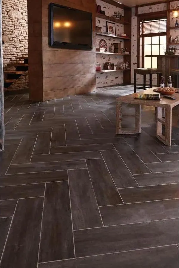 Dark gray groutable tile in a herring bone pattern in a family room with a wood coffee table.