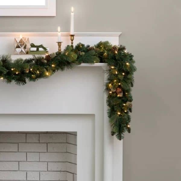 A garland with warm lights hung on a white mantel with candles and gold candlesticks.
